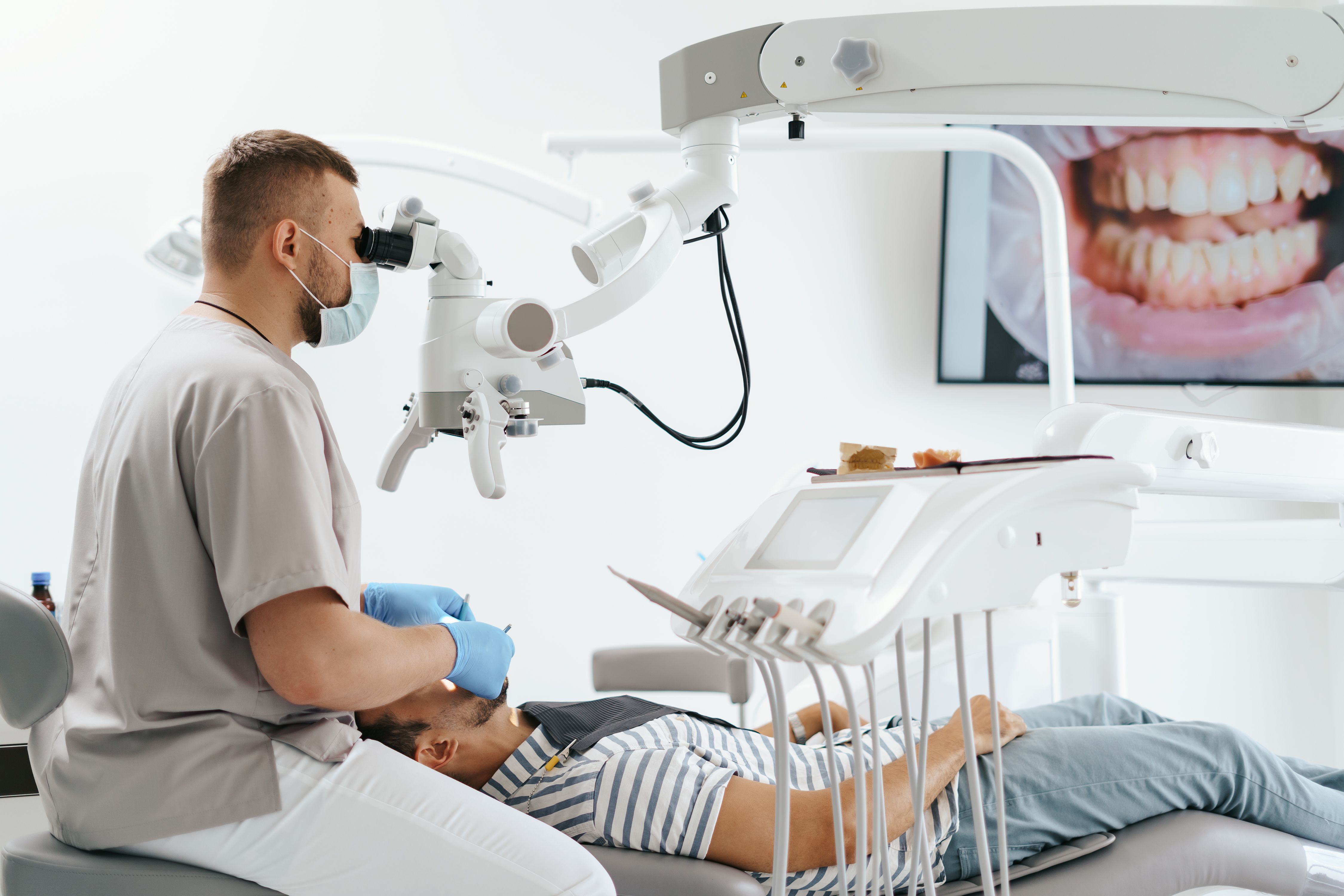 Young Man With Patient Bib Dental Chair Dentist Who Sits Him He Looks His Teeth Using Dental Microscope Holds Dental Bur Mirror